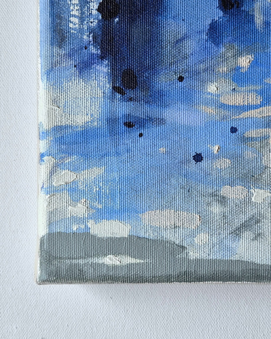Abstract canvas painting with textured impasto brushstrokes in shades of blue, gray, white, and beige, with small black paint splatters, shown close-up against a white wall.