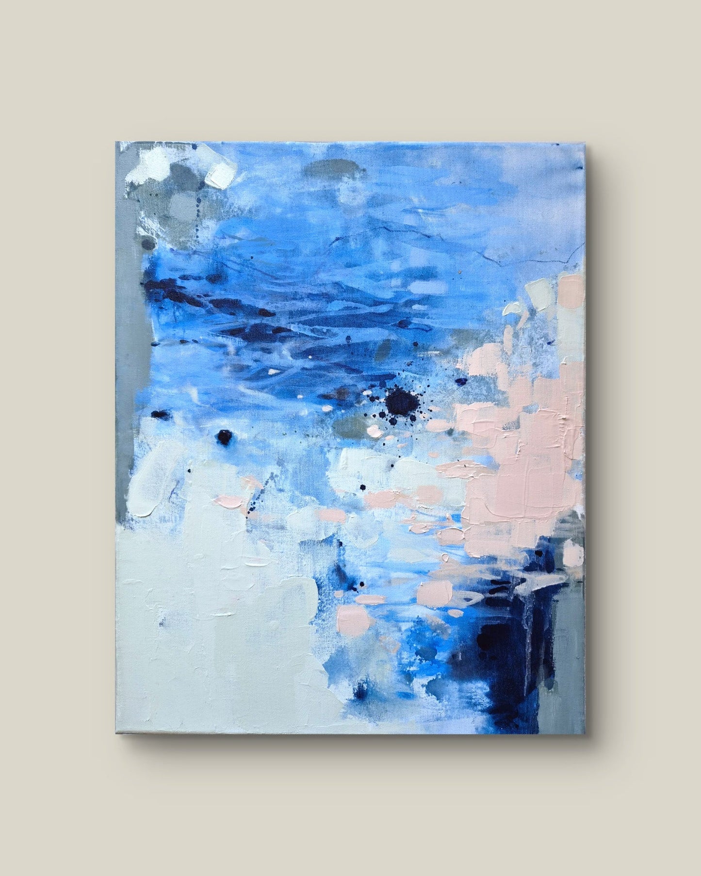 An abstract canvas painting featuring textured brushstrokes of blue, white, light pink, and gray, displayed against a solid beige background.