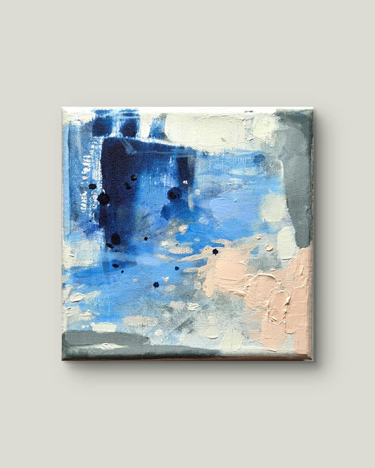An abstract square canvas painting featuring textured brushstrokes of blue, navy, white, gray, and soft peach, displayed against a solid light gray background.
