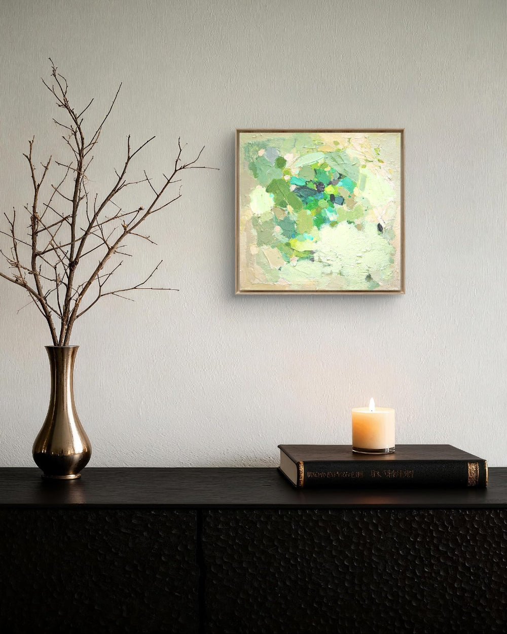 Abstract painting on a wall above a dark surface with a vase, candle, and book.