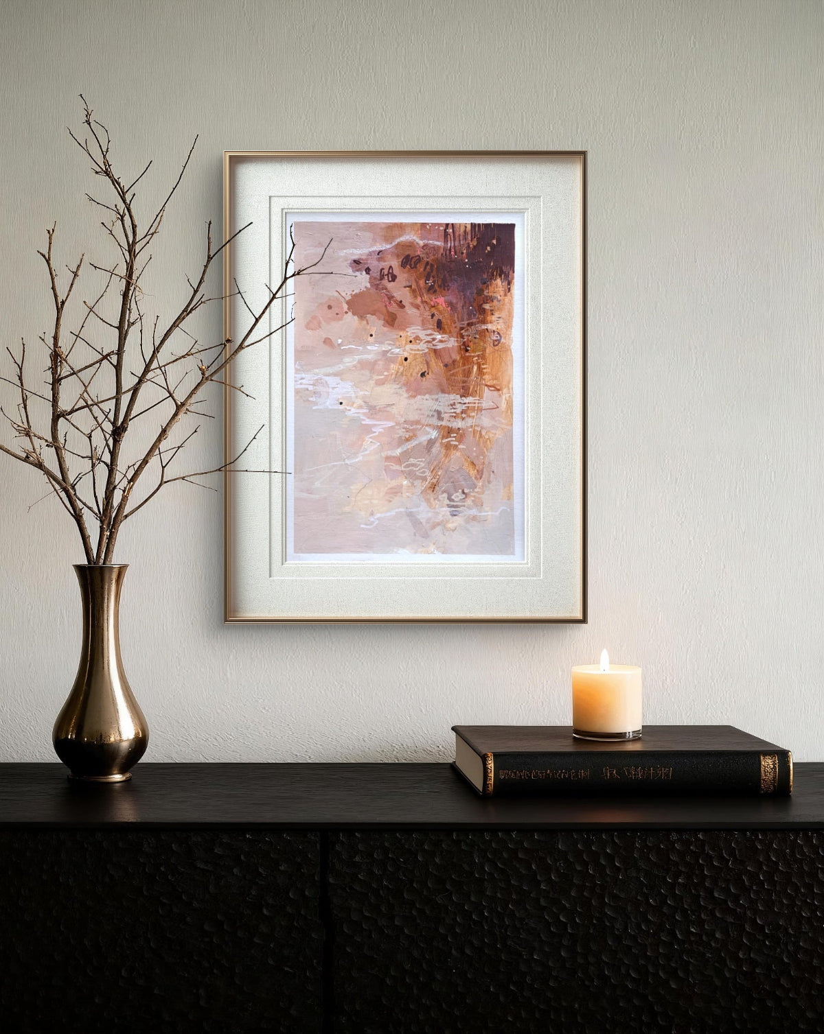 Framed abstract art on a wall with a vase, candle, and book on a shelf below.