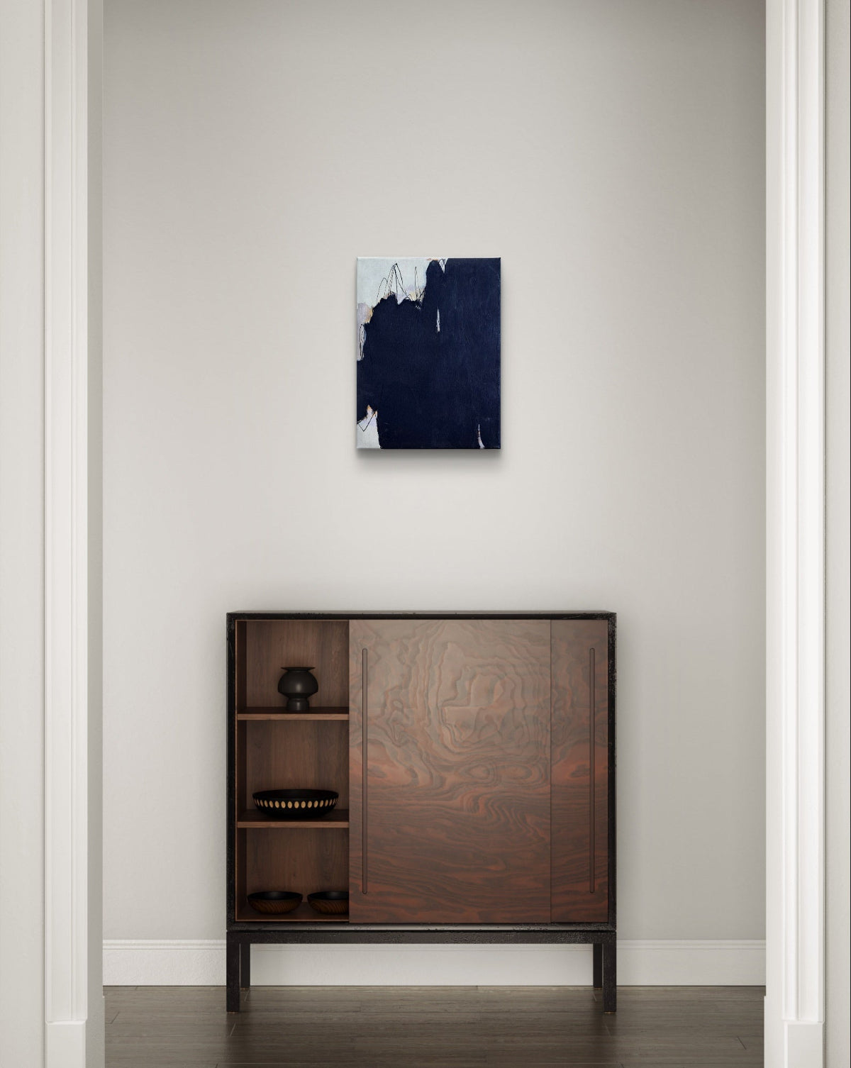 Wooden cabinet with decorative design below a abstract painting on a white wall.