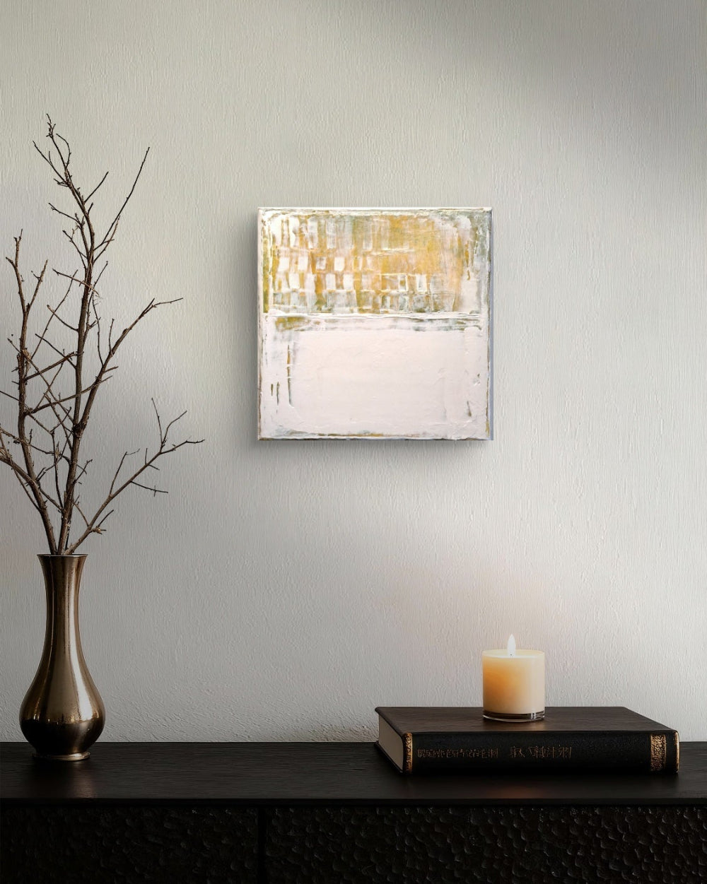 Abstract wall art piece on a gray wall with a candle and vase on a table.